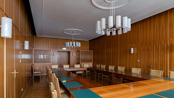 An empty courtroom bench and clerk's desk with a stack of files, seen from the back of a quiet public gallery