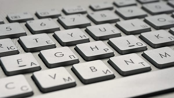 A person holding a phone in one hand and a printed statement in the other beside an open laptop on a desk