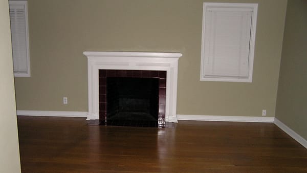 Cardboard moving boxes stacked in an empty room with a rolled rug leaning against the wall near a window