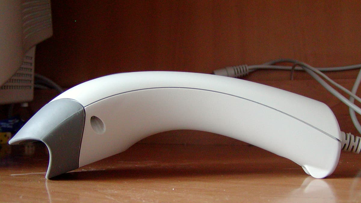 A handheld barcode scanner resting on a supermarket conveyor beside a small stack of grocery items