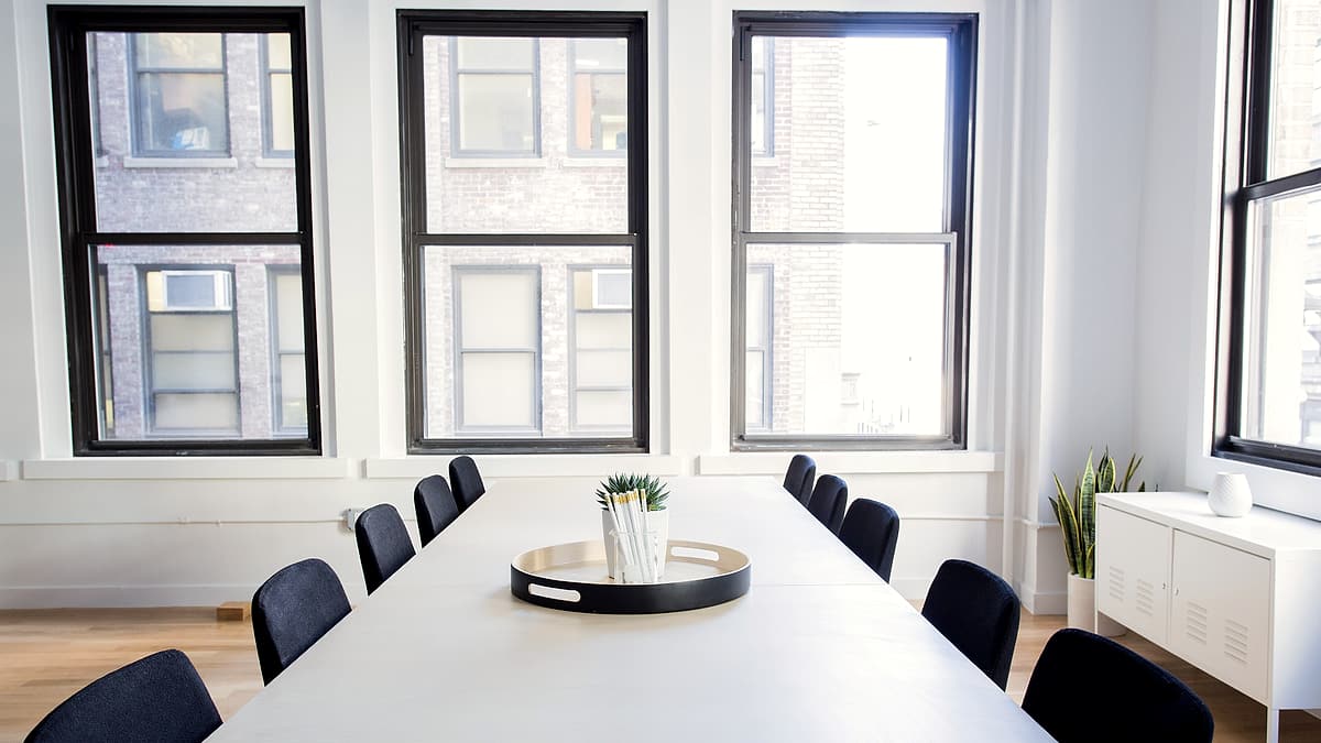 A long conference table with three empty chairs, water glasses, and a small recording device near one place setting