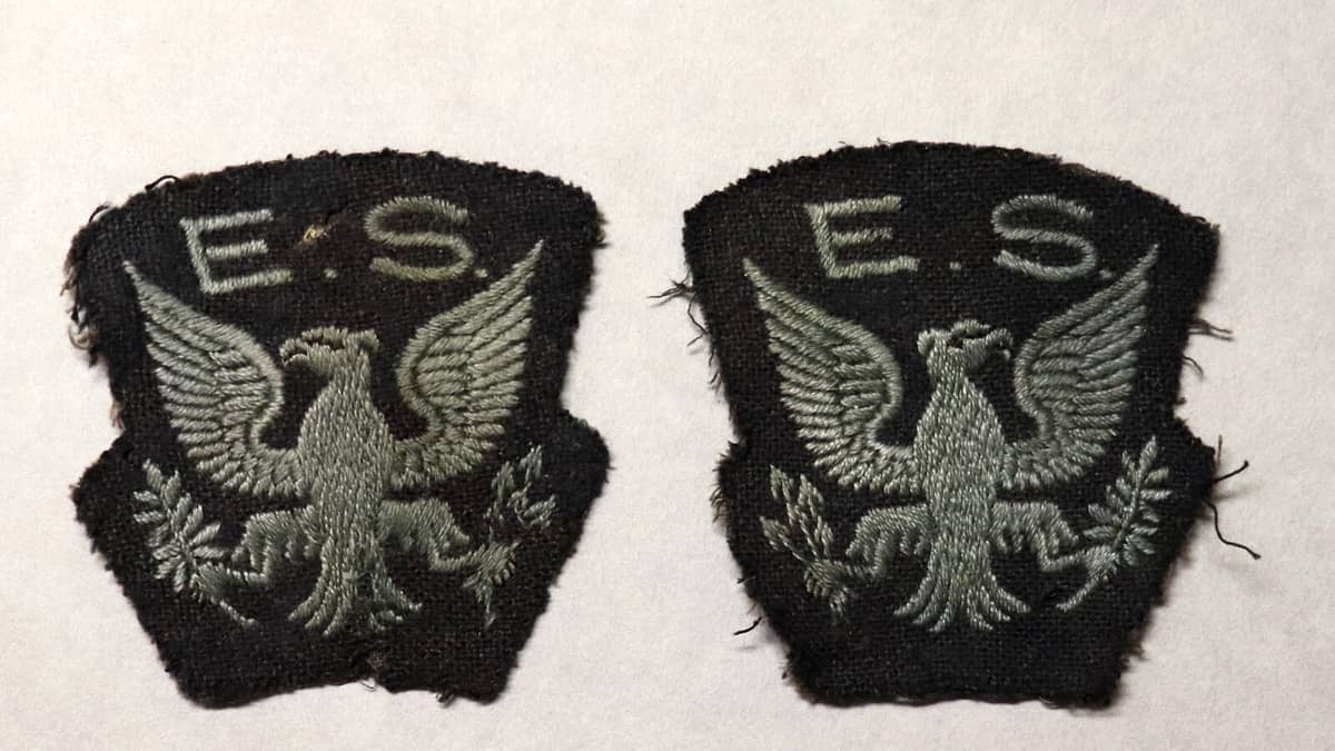 A plain navy uniform shirt on a hanger with an unbranded shoulder patch and empty epaulettes against a locker door